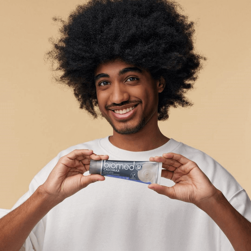 Man holding Biomed toothpaste, smiling and showcasing the best toothpaste for your smile.
