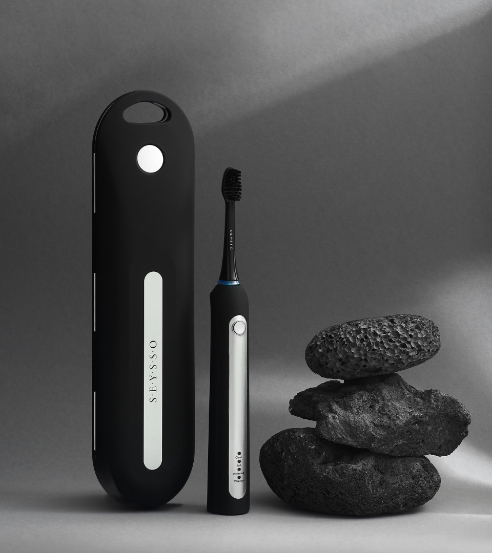 SEYSSO Professional Sonic Toothbrush with Travel Case & Charger next to stacked rocks on a grey background.