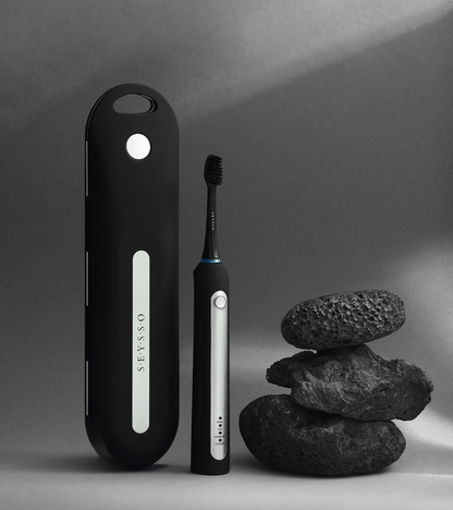 SEYSSO Professional Sonic Toothbrush with Travel Case & Charger next to stacked rocks on a grey background.